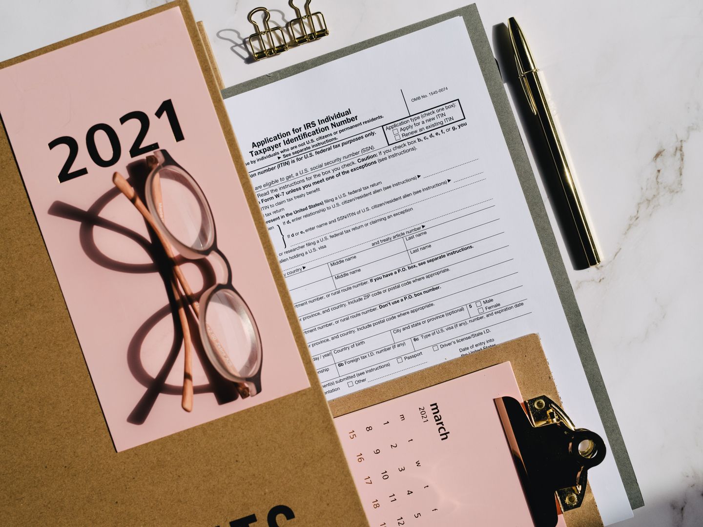 Flat lay of tax forms, calendar, and glasses for 2021 financial planning.